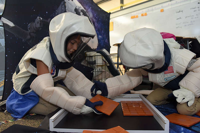 Two children wearing astronaut costumes work together to build a map of mars puzzle